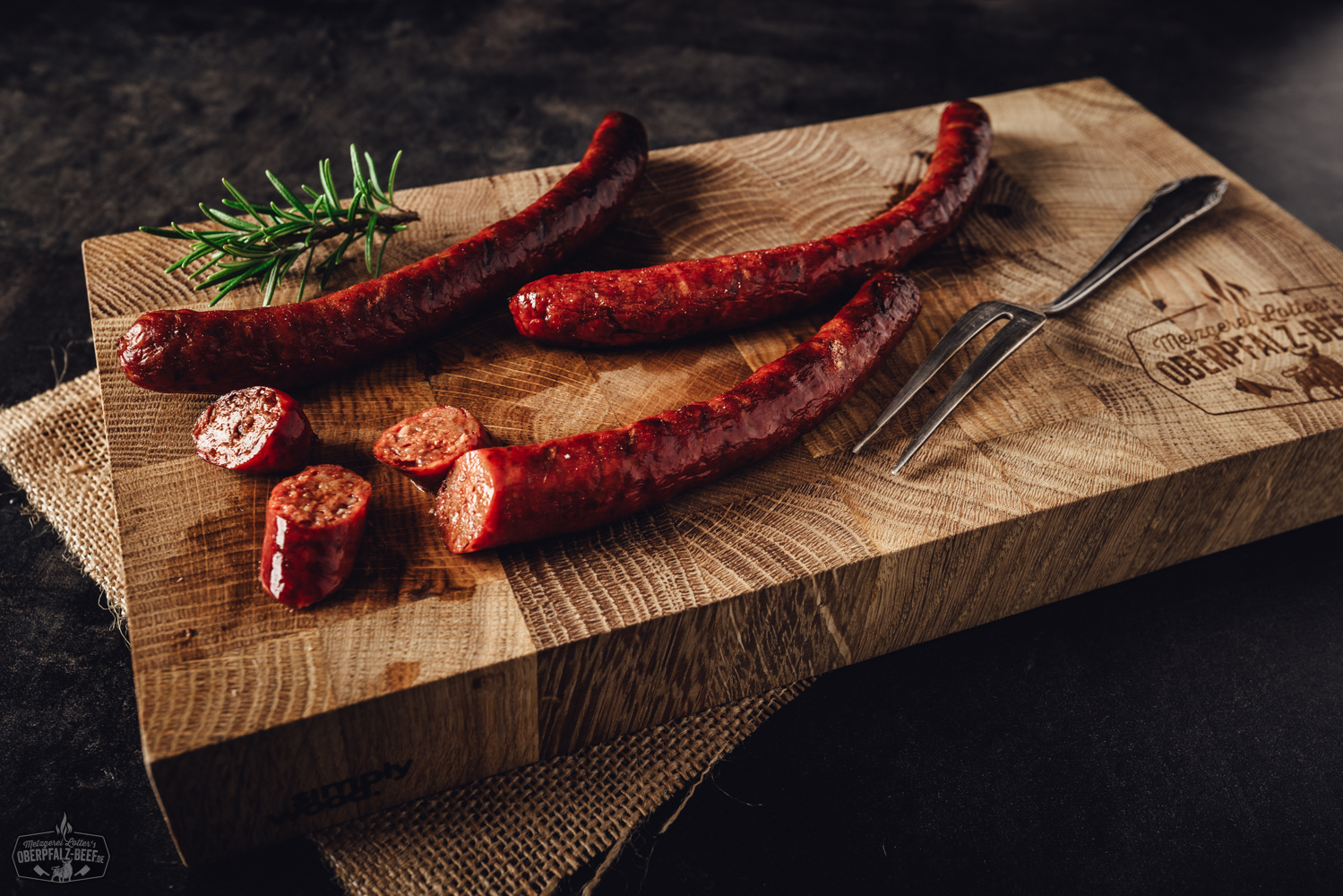 Merguez Bratwürste aus 100% Rindfleisch – würzig, hausgemacht und grillfertig Zwei goldbraun gegrillte Chili-Bratwürste mit sichtbaren Gewürzen liegen auf einem schwarzen Grillrost; im Hintergrund rote Chilischoten und Holzkohle – deftige Spezialität für Grillliebhaber.
