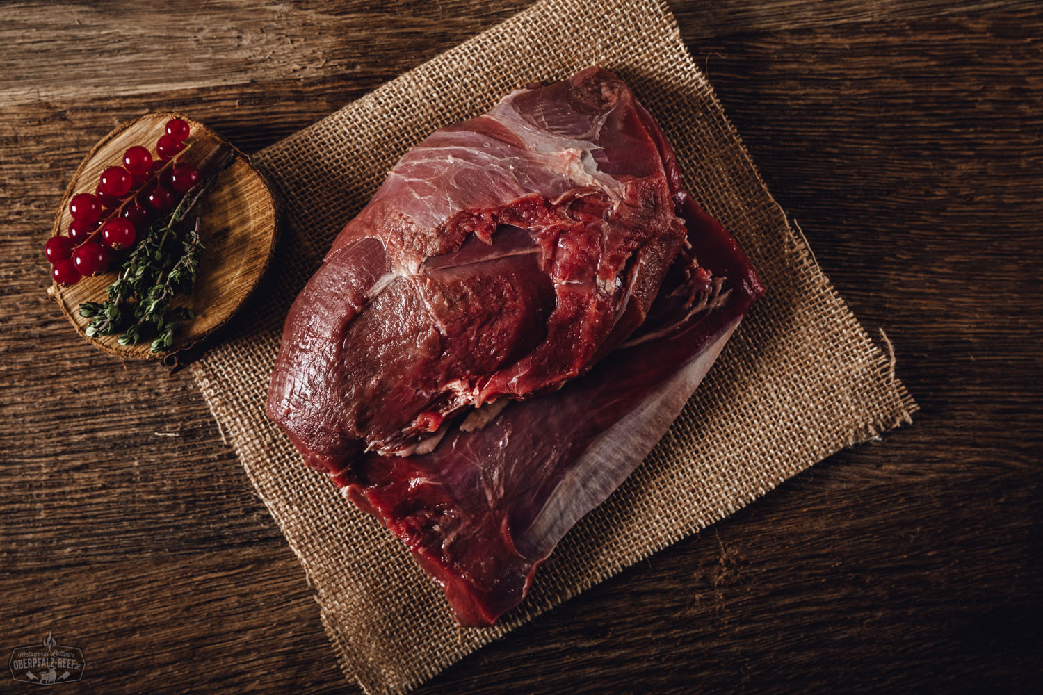 Roher Rehschulter-Braten ohne Knochen aus der Oberpfalz, auf schwarzem Untergrund angerichtet, mit Rosmarinzweig garniert – hochwertiges Wildfleisch für Wildgerichte, regional und nachhaltig produziert.