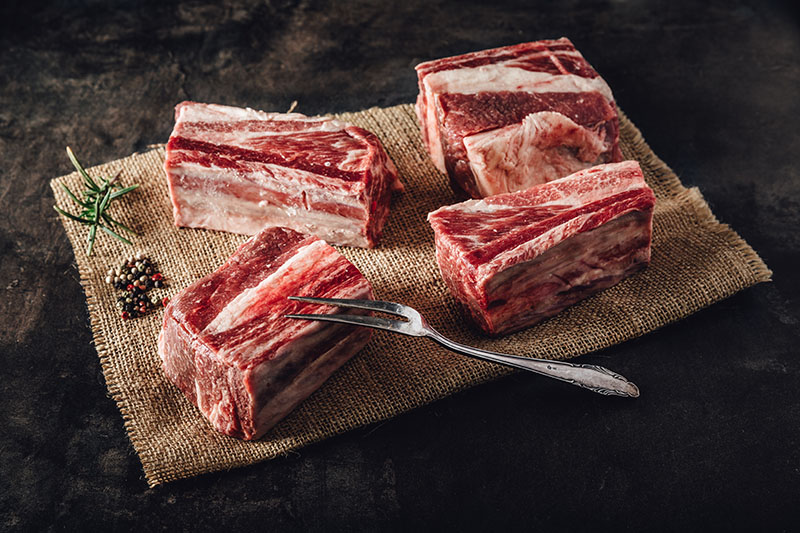 Rohe Querrippe vom Oberpfälzer Rind mit sichtbarer Marmorierung auf dunklem Hintergrund, Fleischstück von hoher Qualität und Frische, ideal zum Schmoren oder Grillen, präsentiert für Direktvermarktung regionaler Rindfleischprodukte.