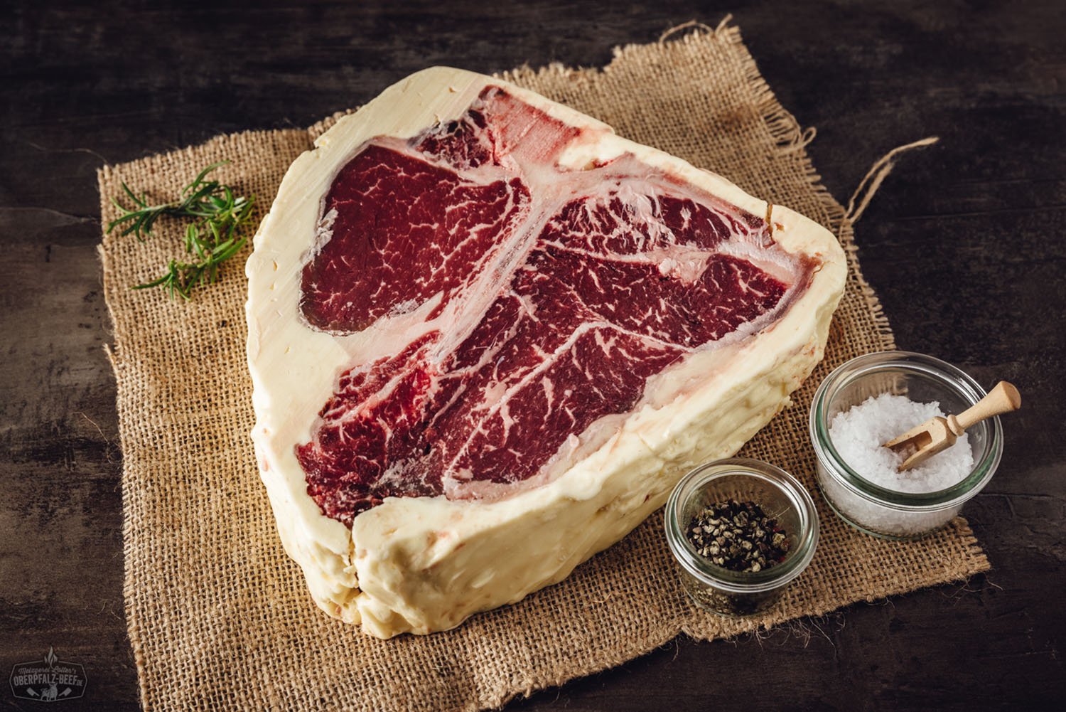 Porterhouse-Steak vom Oberpfalz-Rind, medium gegrillt, mit goldbrauner Fleischkruste, trocken gereift (Butter Aged), auf Holzbrett serviert, daneben frische Rosmarinzweige und Meersalz – hochwertiges Dry-Aged-Steak für Grillgenuss und Fleischliebhaber.