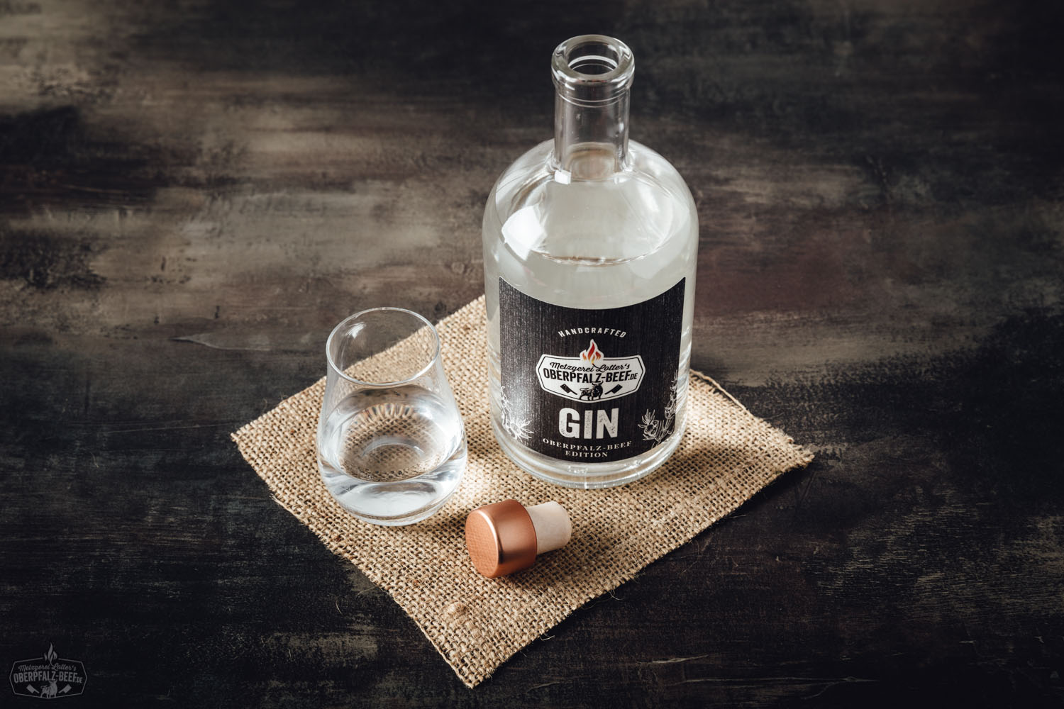 Flasche Handcrafted Oberpfalz Beef Gin auf rustikalem Holzuntergrund, flankiert von Wacholderbeeren, Kräutern und Zitrusfrüchten, stimmungsvoll arrangiert in natürlichem Licht – hochwertiger, regionaler Gin aus der Oberpfalz.