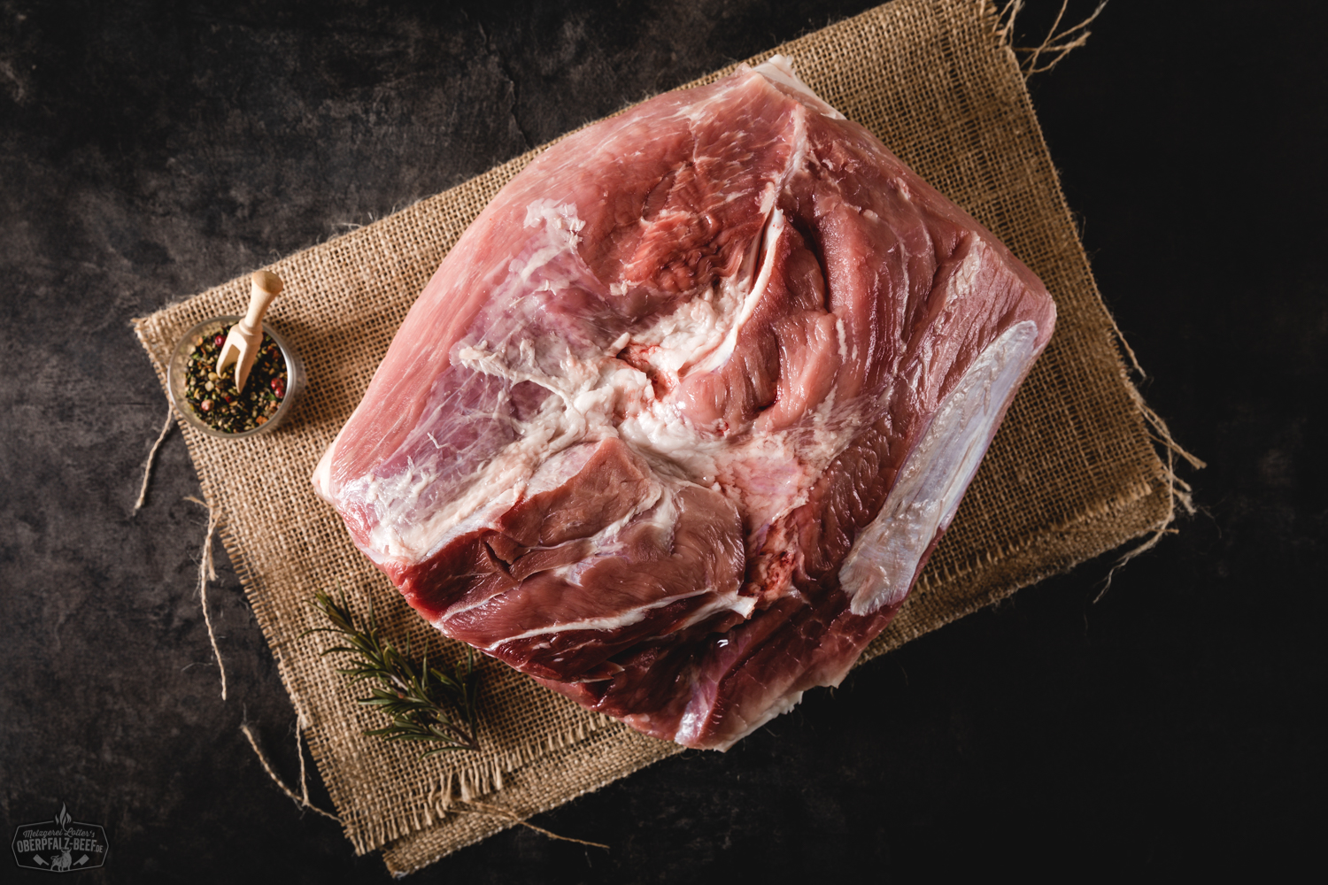 Backschinken gepökelt mit Schwarte vom Oberpfälzer Landschwein – regionales Qualitätsfleisch Rohes Pollo Fino vom Oberpfälzer Bauernhähnchen, ohne Knochen, auf einem dunklen Schneidebrett angerichtet, mit frischen Rosmarinzweigen, Meersalz und Pfefferkörnern garniert – ideale Zutat für saftige Hähnchenrezepte oder Grillgerichte.