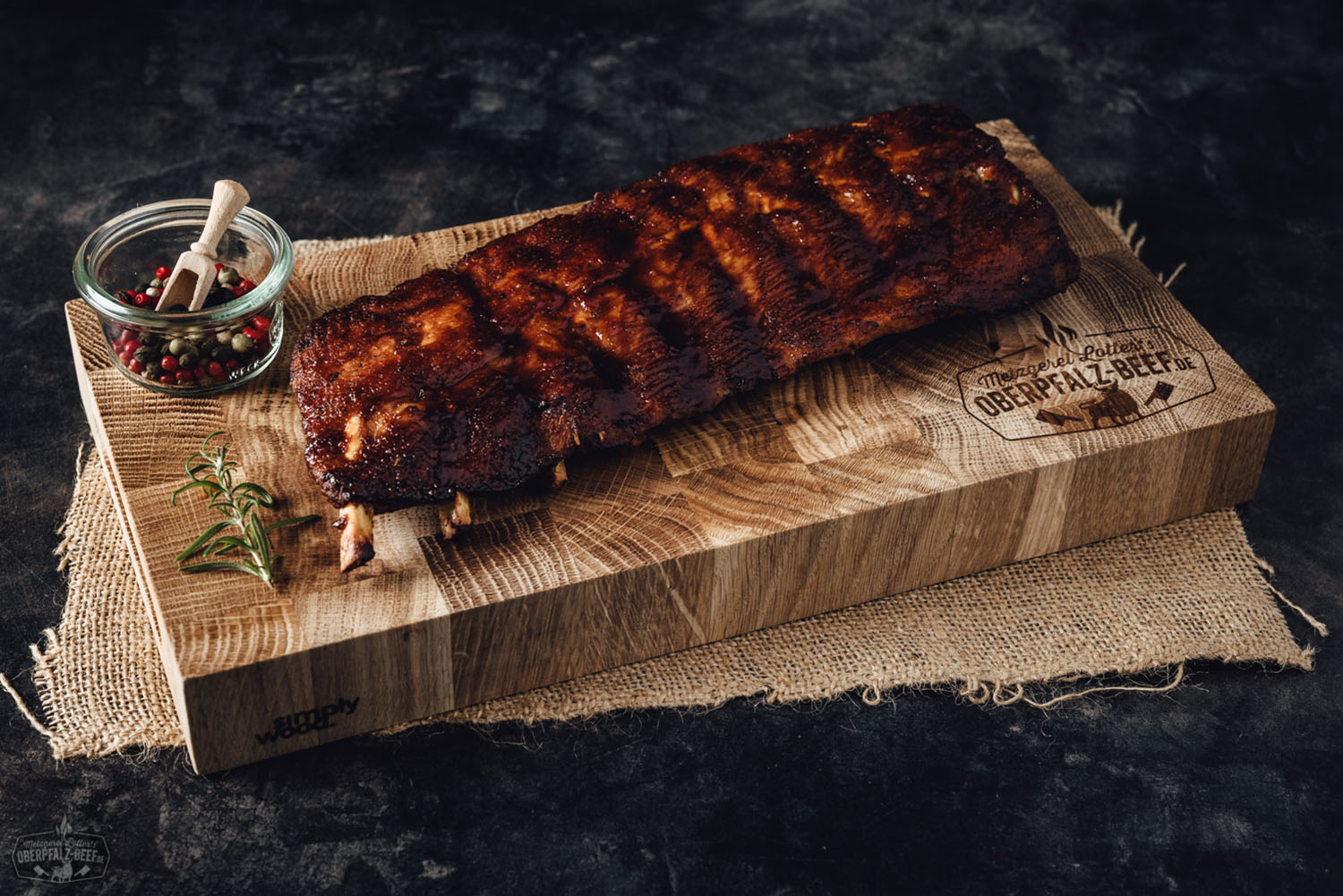 Sous-vide gegarte Baby Back Ribs vom Oberpfälzer Landschwein auf Holzbrett serviert Sous-vide gegarte Baby Back Ribs vom Oberpfälzer Landschwein, zart und saftig mit glänzender BBQ-Glasur, serviert auf einem dunklen Holzbrett mit Rosmarin-Garnitur, perfekt angerichtet für Grill- und Fleischliebhaber.