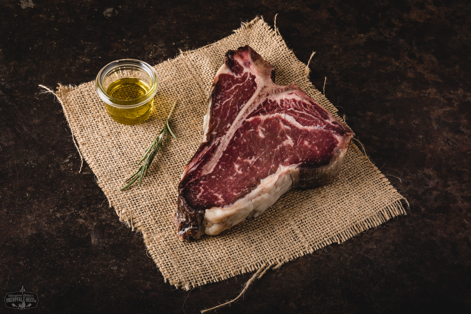 Dry Aged T-Bone Steak vom Oberpfälzer Milchkalb – Premium Fleischqualität Dry Aged T-Bone-Steak vom oberpfälzer Milchkalb auf dunklem Untergrund, roh, marmoriert mit sichtbarem Knochen, hochwertige Fleischstruktur, rustikal präsentiert für Gourmet-Grillen und Fleischliebhaber.