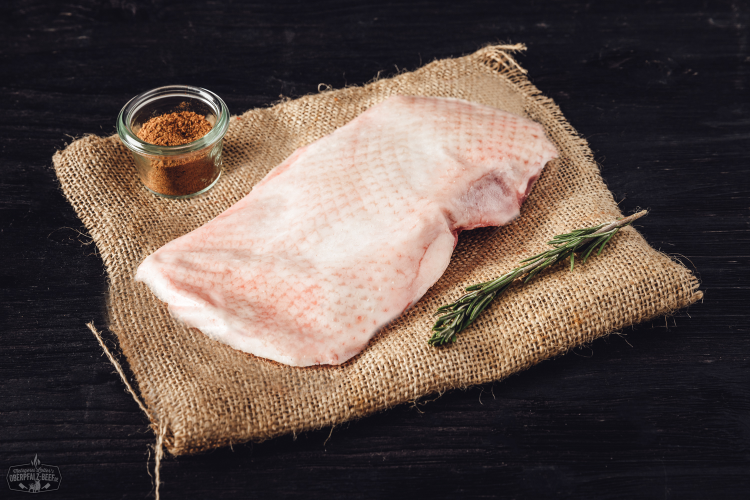 Brustfilet ohne Knochen von der Oberpfälzer Bauerngans – regionales Gänsefleisch in Premiumqualität Zwei Mini-Walnuss-Salamis liegen nebeneinander auf einem dunklen Untergrund; die Salamis sind grobkörnig, mit sichtbaren Walnussstücken durchzogen und teilweise angeschnitten, sodass die Marmorierung und die nussige Struktur deutlich erkennbar sind.