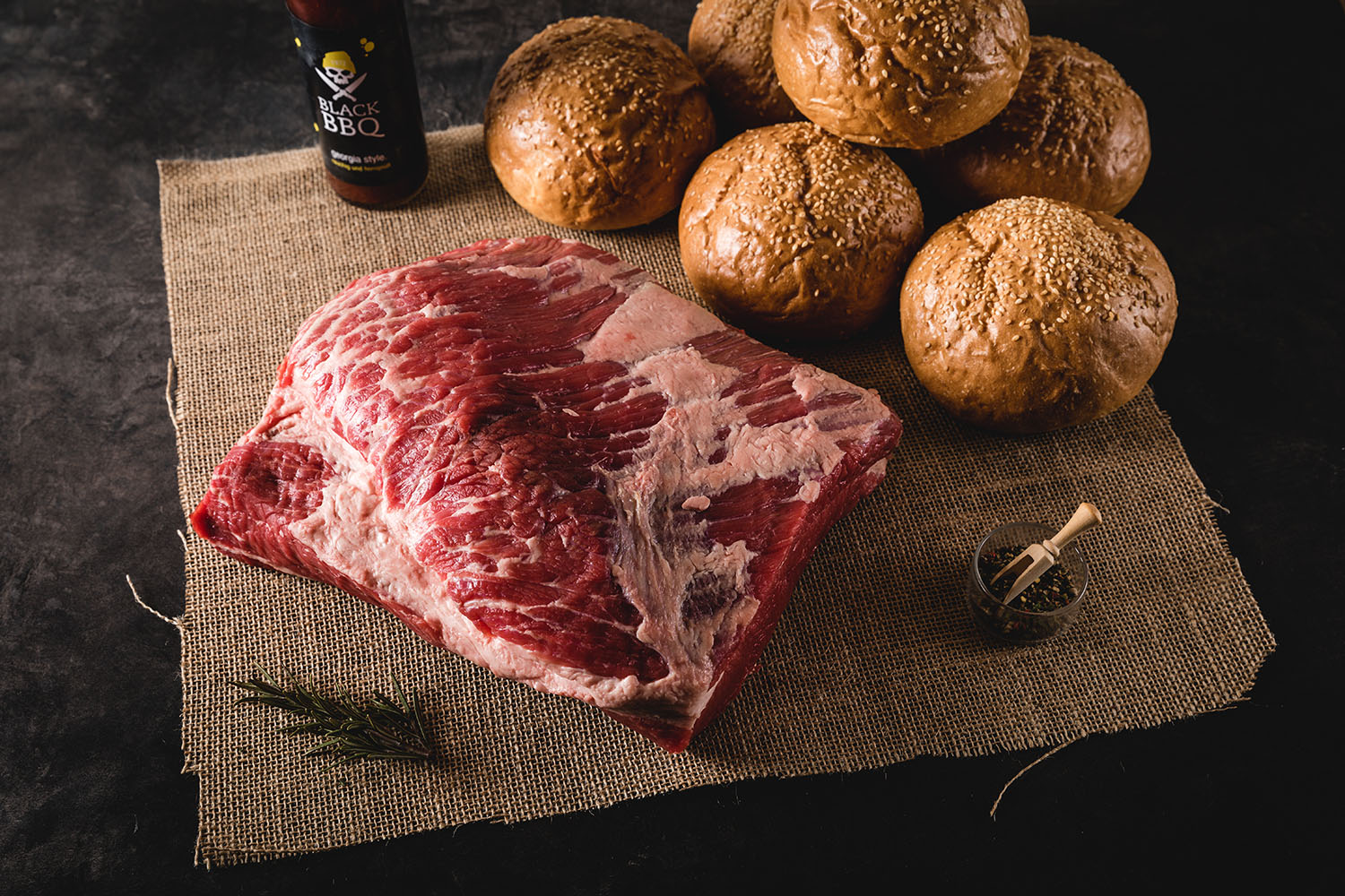 Mehrere Scheiben saftig gegartes Rinderbrustfleisch (Brisket) mit aromatischer Kruste auf einem Holzbrett angerichtet, begleitet von rustikalem Besteck und Gewürzen – perfekte Zubereitung für BBQ-Liebhaber; Produktfoto des Oberpfalz Beef Brisket Pakets.
