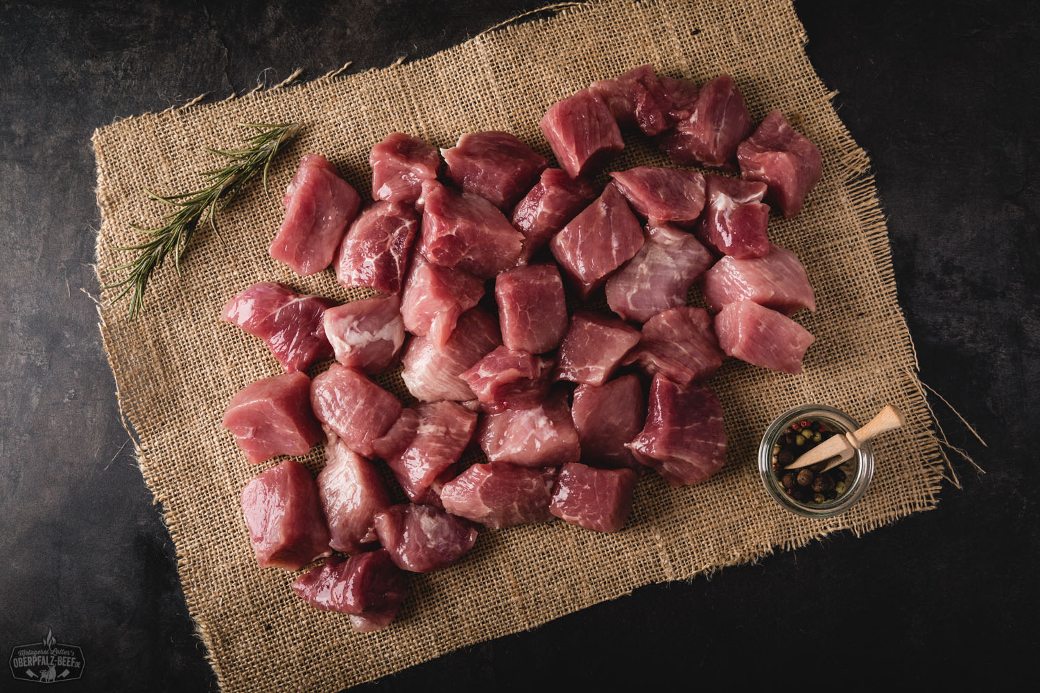 Handgeschnittenes Gulasch vom Oberpfälzer Landschwein – Frisches Schweinefleisch in Premium-Qualität Handgeschnittenes Gulasch vom Oberpfälzer Landschwein, roh und in gleichmäßige Stücke geschnitten, auf dunklem Holzuntergrund präsentiert – frisches Schweinefleisch aus regionaler Herkunft, ideal für deftige Schmorgerichte.