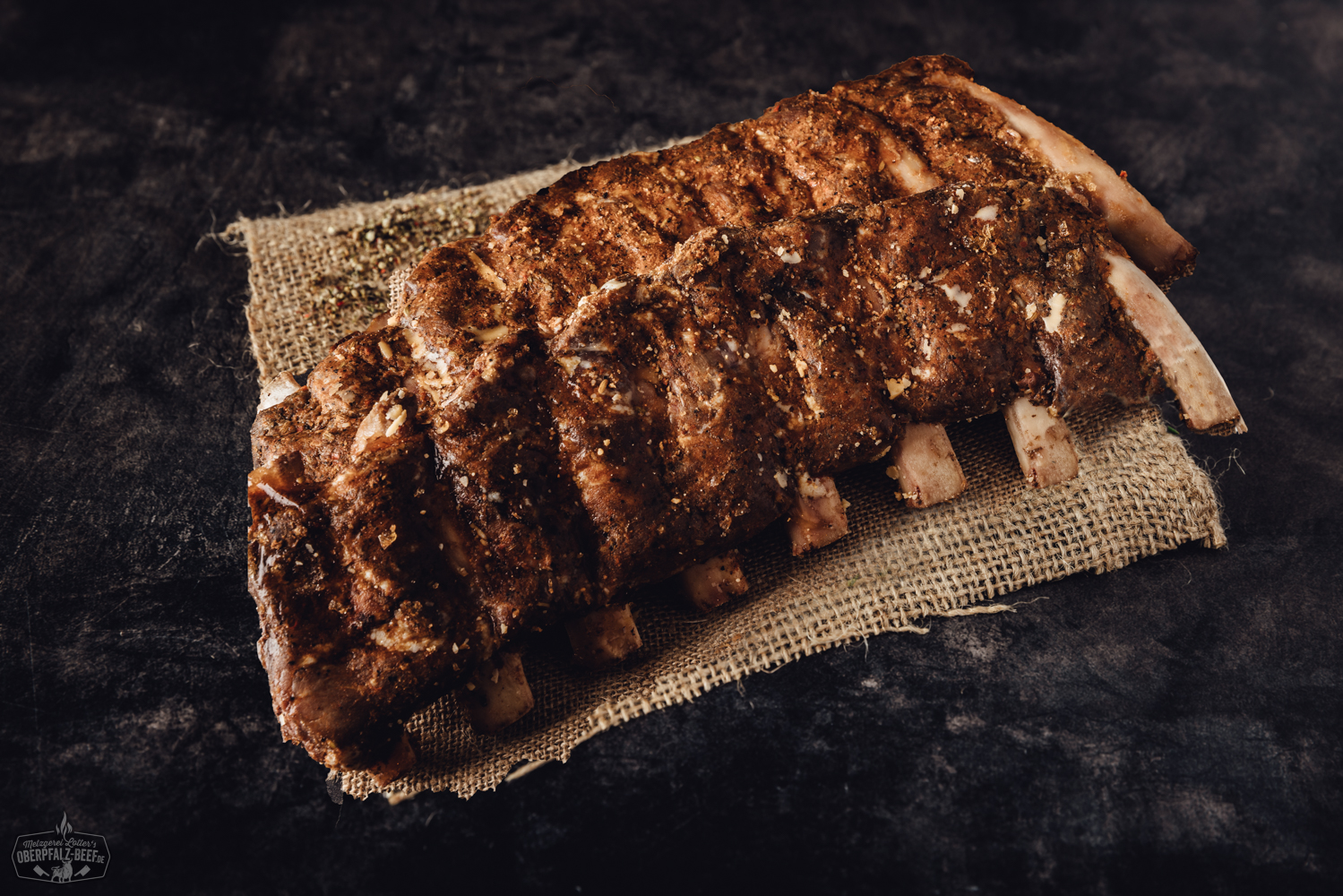 Sous-vide gegarte Beef Back Ribs vom Oberpfalz-Rind auf Schneidebrett mit BBQ-Sauce Sous-vide gegarte Beef Back Ribs vom Oberpfalz-Rind, saftig und zart mit dunkler BBQ-Glasur, angerichtet auf einem Holzbrett mit frischen Kräutern und Gewürzen, rustikaler Hintergrund – perfekte Grill-Delikatesse für Fleischliebhaber.