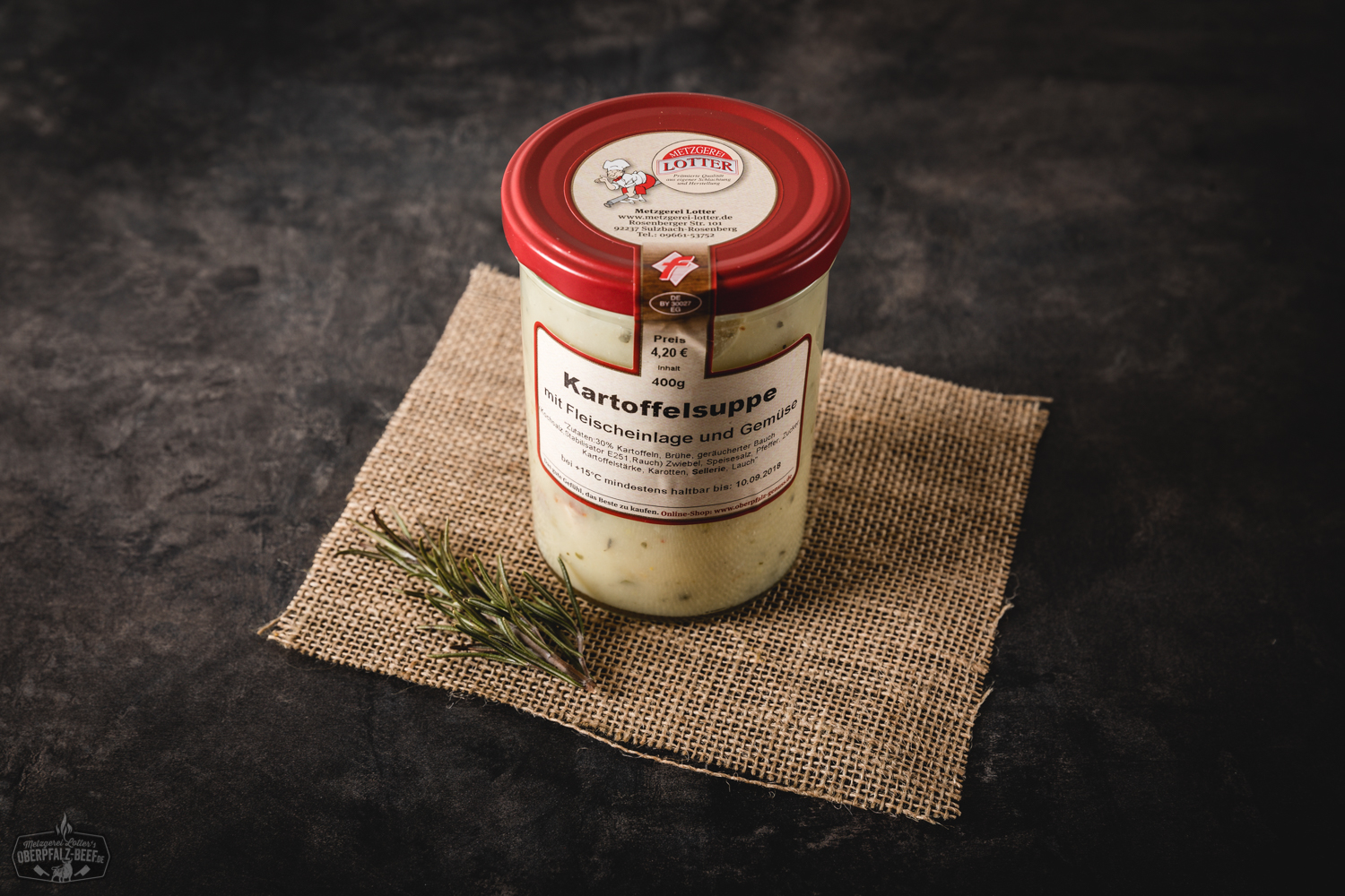 Hausgemachte Kartoffelsuppe im Glas mit Wurststückchen, dekorativ angerichtet auf einem Holztisch mit frischen Kräutern – deftige bayerische Spezialität im Einmachglas.