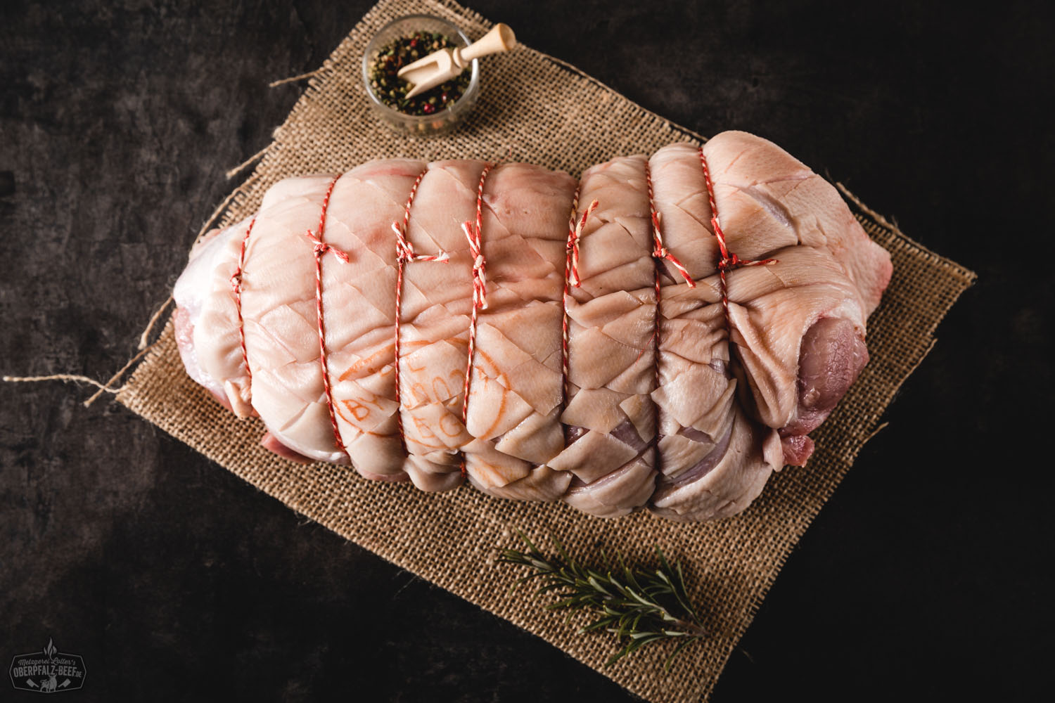 Gerollte Spanferkelschulter vom Oberpfälzer Landschwein, goldbraun gebraten mit knuspriger Kruste, angerichtet auf einem Holzbrett, im Hintergrund Kräuter und rustikale Küchendekoration – traditionelle bayerische Spezialität.