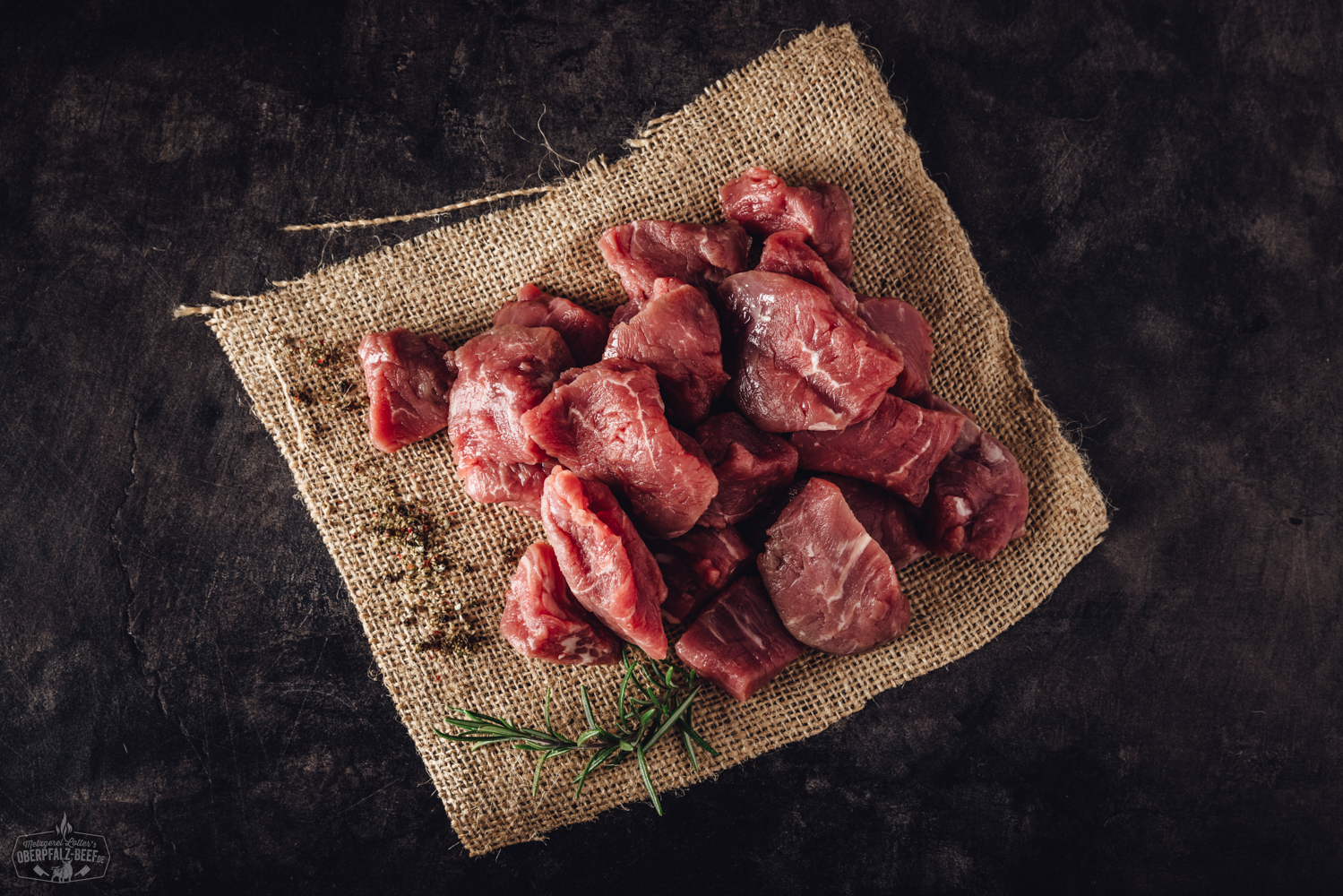 Handgeschnittenes Rinderfilet für Fondue – Premium Beef aus der Oberpfalz Handgeschnittenes Rinderfilet-Fonduefleisch roh auf einem Holzbrett angerichtet, umgeben von frischen Kräutern, rosa Pfefferkörnern und grobem Meersalz – hochwertige Zubereitung für Fondue oder Grillgerichte.