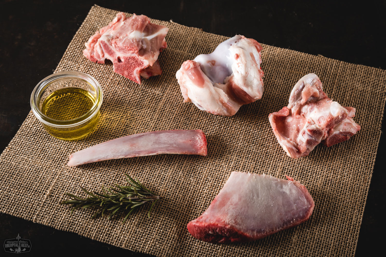 Rohe Kalbsknochen vom Oberpfälzer Milchkalb, frisch präsentiert auf einem dunklen Brett mit leichtem Marmormuster, ideal zur Zubereitung von Knochenbrühe oder Suppe; regionale Metzgerqualität aus der Oberpfalz.