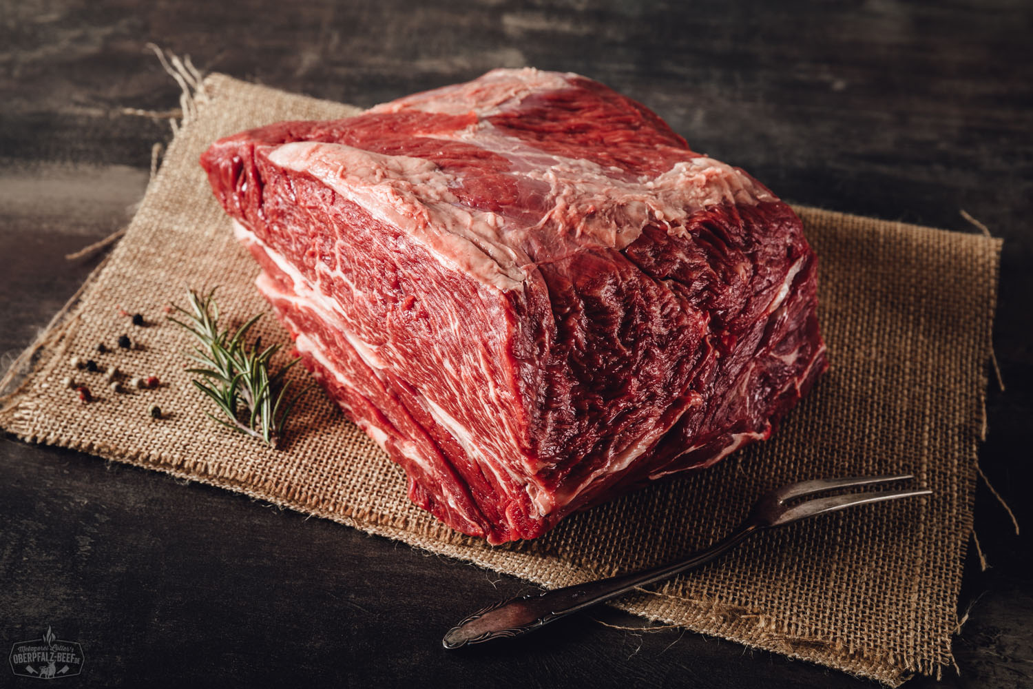 Rohes Suppenfleisch aus der Wade vom Oberpfalz-Rind auf einem dunklen Schneidebrett, umgeben von frischem Gemüse wie Karotten, Lauch und Sellerie, dekorativ angerichtet zur Zubereitung einer traditionellen Rinderbrühe.